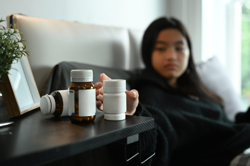 Young woman taking medicines from bedside table to relieve symptoms.